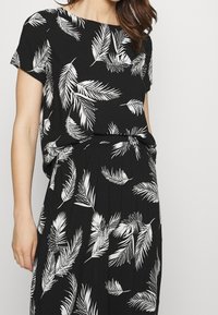 Černé šaty s volným střihem, krátkými rukávy a bílým listovým vzorem. Vyrobeno z měkkého materiálu s uvolněným siluetou.