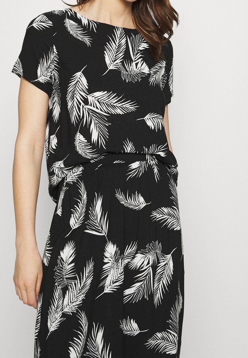 Černé šaty s volným střihem, krátkými rukávy a bílým listovým vzorem. Vyrobeno z měkkého materiálu s uvolněným siluetou.