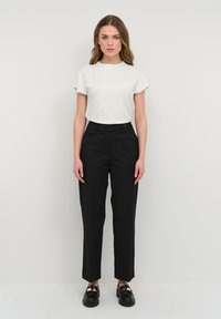 Top bianco a maniche corte abbinato a pantaloni neri su misura con taglio dritto, bottone in vita e tasche frontali piatte. Scarpe nere con finitura lucida.
