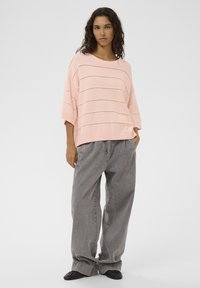 Hellrosa gestrickter Pullover mit horizontalen Streifen und weiten Ärmeln, kombiniert mit grauer, locker sitzender Hose und schwarzen Schuhen.