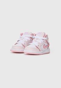 Para małych, białych i różowych trampków dla malucha z sznurowadłami oraz logo Nike na jednolitym jasnym tle.