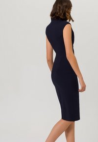 Marinblå kroppsnära klänning med hög krage, korta ärmar och knälång fåll. Släkt tyg med en elegant silhuett.