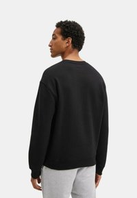 Sudadera negra con cuello redondo y puños acanalados, que presenta un corte relajado y una textura suave. Detalles de costura visibles en los hombros y la parte posterior.