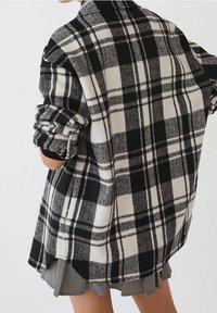Chaqueta de camisa a cuadros en blanco y negro con textura cepillada, forma sobredimensionada, mangas dobladas y un dobladillo ligeramente curvado.