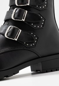 Svart fusk läderstövel med tre justerbara silver spännen och nitar. Kraftig, mönstrad sula och slät textur.