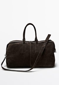 Hnědá semišová taška typu duffle s dvojitými držadly, nastavitelným ramenním popruhem a kontrastním prošíváním. Má zipové uzavírání a obdélníkový tvar.
