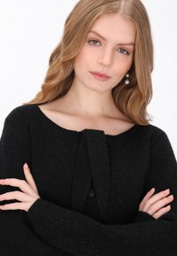 Pulover negru dintr-un tricot moale, cu decolteu rotund, având un detaliu cu fundă în față și mâneci lungi. Textură plăcută, cu un aspect ușor pufoș. 