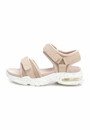 Sandalias de tela beige con un diseño de dos correas y cierres ajustables, que cuentan con una suela gruesa moteada en blanco y amortiguación de aire.