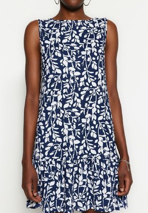 Marineblauwe mouwloze jurk met een wit bladerenpatroon, voorzien van een gestructureerde stof en een gelaagde gerafelde zoom.