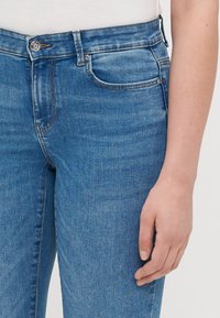 Vaaleansiniset farkut, joissa on istuva muotoilu, viisi taskua, hienovaraista kulumista ja napitus vyötäröllä.