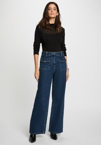 Haut noir à manches longues avec un col côtelé ; pantalon en denim bleu taille haute à jambes larges avec deux poches avant et une taille ajustée.