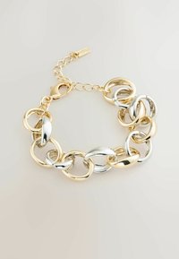 Bracciale con anelli ovali grandi alternati in oro e argento e chiusura a catena dorata su uno sfondo chiaro.