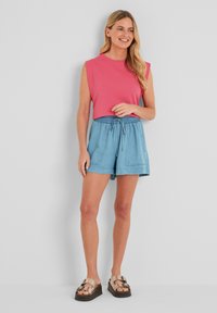 Sleeveless pink top with a round neckline, paired with light blue drawstring shorts. Outfit completed with tan platform sandals.