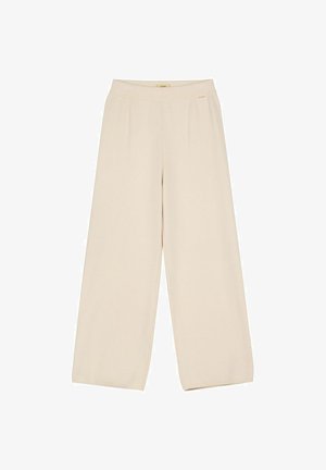 Beżowe spodnie z szerokimi nogawkami, wysokim stanem i małą złotą metką marki u góry na białym tle.