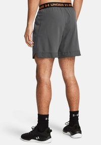 Pantalones cortos deportivos grises con una cinturilla elástica que presenta un logo naranja. La tela parece ligera y transpirable, con una sutil textura.