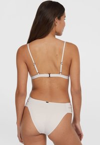 Ensemble de bikini beige clair avec bretelles spaghetti réglables, fermeture à crochet et bas taille haute ornés d'accents décoratifs sur les côtés.