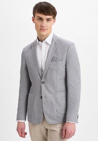 Hellgrauer Blazer mit strukturiertem Muster, zwei Vorder Taschen, Ein-Knopf-Verschluss und einem dekorativen Einstecktuch. Kombiniert mit einem weißen Hemd.