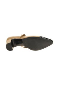 Zapato de tacón beige con punta afilada y correa ajustable. La suela es de goma negra con un acabado suave. Acentuado con un detalle dorado.