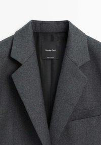 Mørkegrå uldjakke med reverskrave, enkelt brystlomme og ensfarvet foring. Mærket siger "Massimo Dutti."