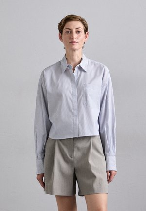 Raidoitettu nappikauluspaita vaaleansinisessä ja valkoisessa, jossa on rintatasku, yhdistettynä harmaisiin muotovaltaisiin shortseihin. Kankaan pinta on sileä ja istuvuus rento.