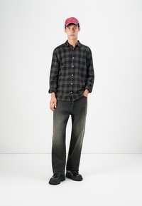Camisa de franela a cuadros en blanco y negro, jeans grises y zapatos negros gruesos. Lleva puesto un gorro rojo. Diseño simple, casual y de corte relajado.