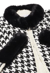 Svartvitt houndstooth-mönstrad kappa med faux fur-krage och ärmar. Har en gulddekorerad dragkedja med läderdetaljer.