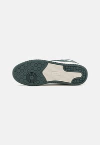 Podeszwa zielono-białego sneakersa z okrągłymi i liniowymi wzorami bieżnika oraz logo "hummel" na beżowej środkowej części.