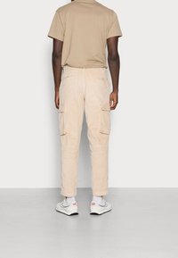 Beige kordflorsbyxor med två sidofickor, slim fit och elastiska muddar. Bärs med en ljusbrun t-shirt och vita sneakers.