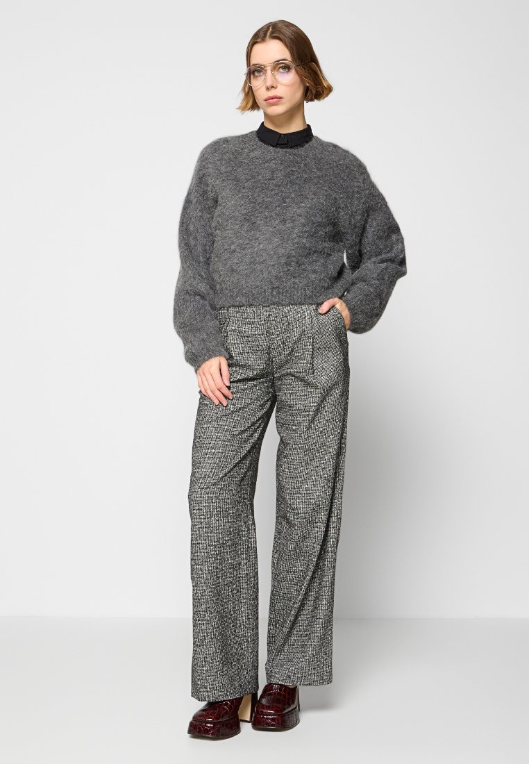 Grauer Mohair-Pullover mit voluminösen Ärmeln, kombiniert mit hoch taillierten gemusterten Hosen in Schwarz und Weiß. Braune glänzende Mokassins runden den Look ab.