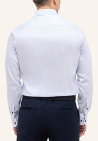 Camicia a righe azzurro chiaro con maniche lunghe e polsini con bottone. Presenta un colletto classico ed è abbinata a pantaloni blu navy.