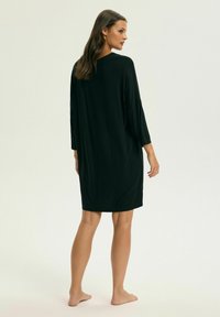 Czarna, luźna sukienka wykonana z miękkiego materiału, z rękawami o długości trzech czwartych i luźnym krojem, sięgającą do połowy uda.