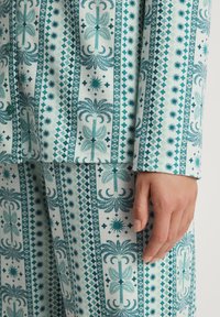 Patroong loungewear in lichte stof met teal palmboom- en geometrische motieven op een witte achtergrond. Inclusief knopen en manchet-details.