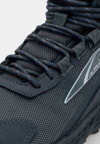 Sorte løpesko med teksturert mesh-overdel, reflekterende detaljer og forsterkede snørehull med tykke lisser for sikker passform.
