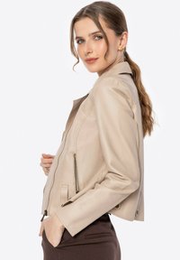 Beige faux leren jack met een getailleerd ontwerp, met ritszakken en een gladde textuur. Minimalistische stijl met een kortere lengte en drukknoopsluiten.