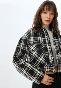 Sorte og hvide plaid cropped jakke med tekstureret stof, store frontlommer og sorte knapper. Lange ærmer og en boxy form.