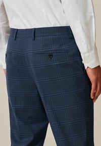 Navy checkered trousers made of textured fabric, featuring two back pockets with black buttons and a slim-fit design.