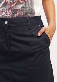 Gonna di un blu scuro realizzata in tessuto misto cotone, con tasche laterali, chiusura con bottone in metallo e dettagli di cucitura a vista.