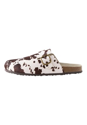 Mule sans lacets avec imprimé vache marron et blanc, bride réglable avec boucle, semelle intérieure en liège et semelle extérieure noire texturée, vue de côté.