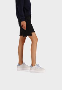 Sneaker platform bianchi con accenti blu chiaro, indossati con una gonna in denim nera con orlo sfilacciato. Stile atletico casual.