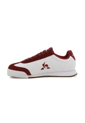 Zapatilla baja blanca y rojo oscuro con cordones y un logo en el lateral, con suela de goma plana y forro de tela.