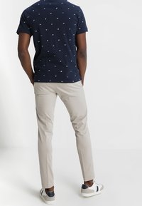 Polo bleu marine avec petits motifs blancs, chinos beige coupe slim et baskets blanches avec détails bleu marine. Tissu lisse et coupe ajustée.