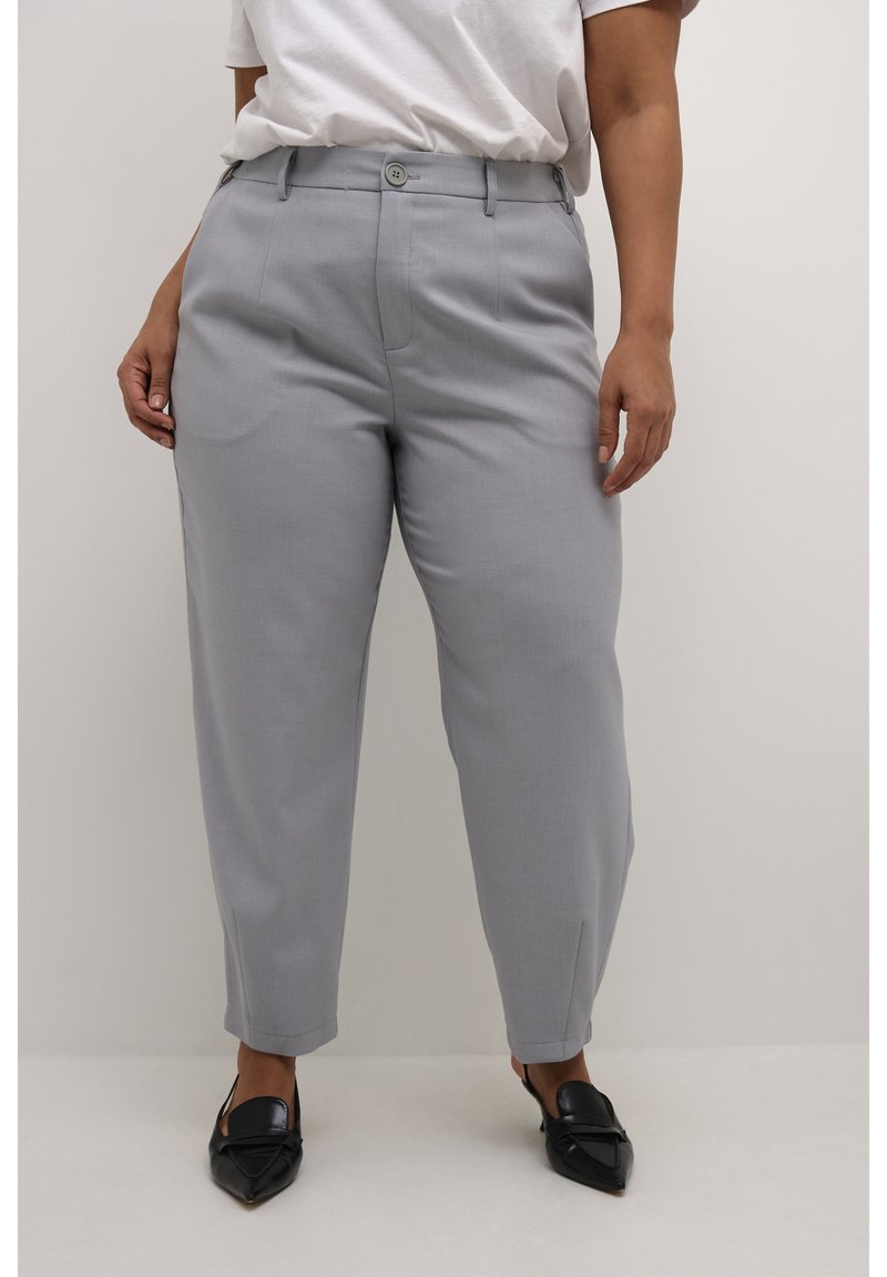 Pantaloni grigi su misura dal taglio dritto, con pence piatte, tasche laterali e sottili spacchi sull'orlo, abbinati a mocassini neri con punta appuntita.