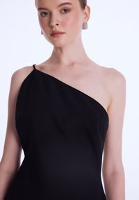 Černé šaty jednoho ramene s hladkou strukturou, zdobené volným designem a jemným detailem ramínka, které představují elegantní, minimalistický styl.