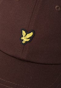 Casquette marron en tissu texturé, ornée d'un logo d'oiseau brodé jaune à l'avant avec un contour noir.
