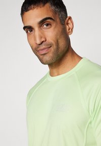 Light green athletic shirt with short raglan sleeves, featuring a subtle logo on the chest and a textured fabric surface.