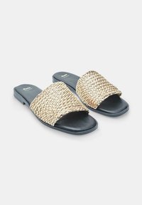 Kudotut liukujalkaiset sandaalit leveällä kultaisella ja beige hihnalla, musta sileä pohja ja tasainen korko. Ominaisuuksina monimutkainen kuvio ja minimaalinen muotoilu.