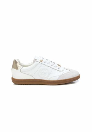 Zapatilla blanca de caña baja con puntera de ante beige, talón metálico dorado, cordones blancos, logo lateral en relieve y suela de goma marrón.