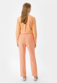 Różowa bluzka z długim rękawem i pasującymi szerokimi spodniami, wykonana z gładkiego materiału, z tylnymi kieszeniami i luźnym krojem.