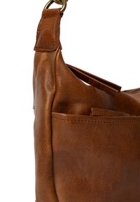 Sac à épaule en cuir marron avec une texture douce, présentant un design incurvé, un anneau en métal et des détails de poches externes.