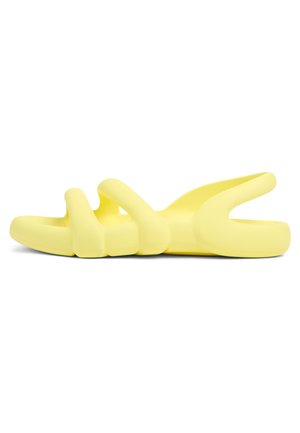 Yellow slide sandal made of soft material. Design features curved straps and a thick sole for comfort. Smooth texture and minimalist shape.